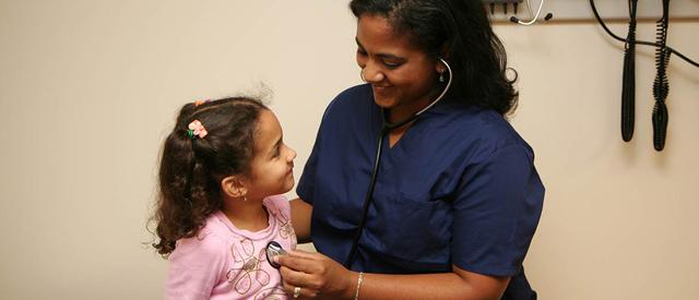 A healthcare professional gently examines a smiling young child with a stethoscope during a routine checkup.